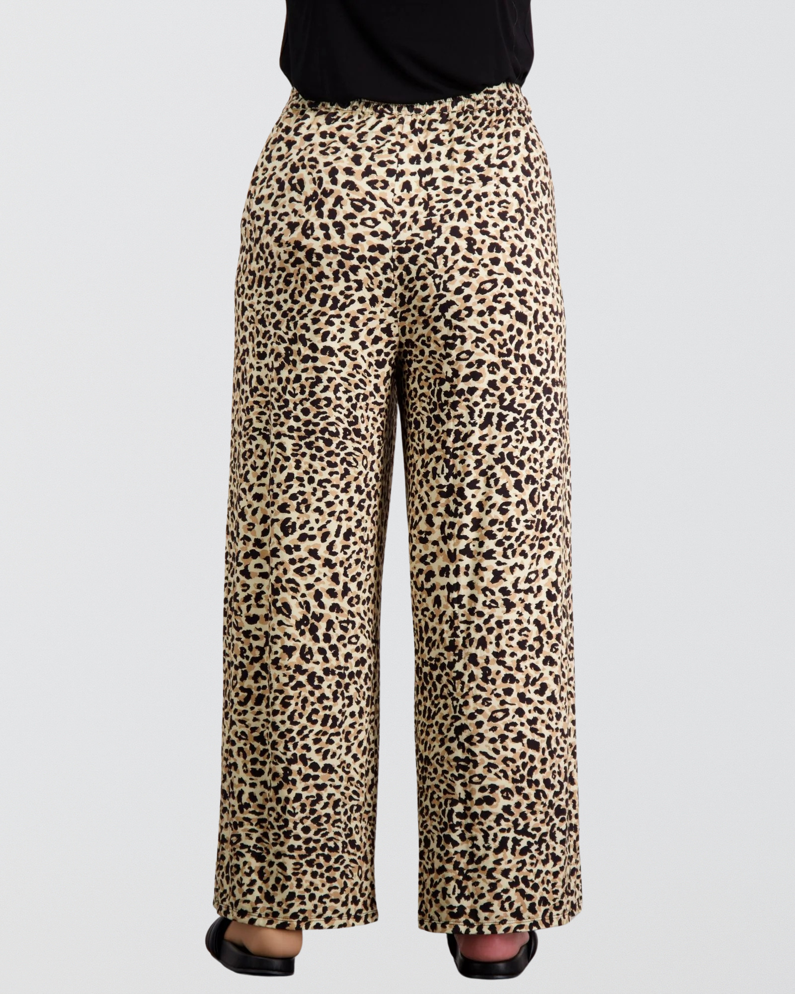 Jessie Wide Leg Pant features a stylish leopard print pattern on beige background, showcasing a relaxed, flowing silhouette with full-length wide legs. The adaptive comfort pants are shown paired with a black top and sandals, highlighting their versatile and comfortable design.