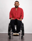 A person in a wheelchair wearing the Stephen Seated Jeans in black, paired with a vibrant red button-up shirt with rolled sleeves. The adaptive jeans feature a comfortable seated design. The model is photographed against a light background, showcasing the casual yet stylish ensemble.