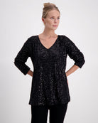 Tara V Neck Leaf Back Top in shimmering black metallic glitter fabric with long sleeves. Featuring a flattering V neckline, relaxed fit, and signature leaf pattern on the back. Perfect evening wear top with stretch sequin detail against light studio background.