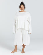 The Essensual PJ Set features a flowy white two-piece sleepwear ensemble with a loose-fitting long-sleeve top and cropped wide-leg pants, photographed against a light gray background, showcasing comfortable adaptive sleepwear design and relaxed silhouette.