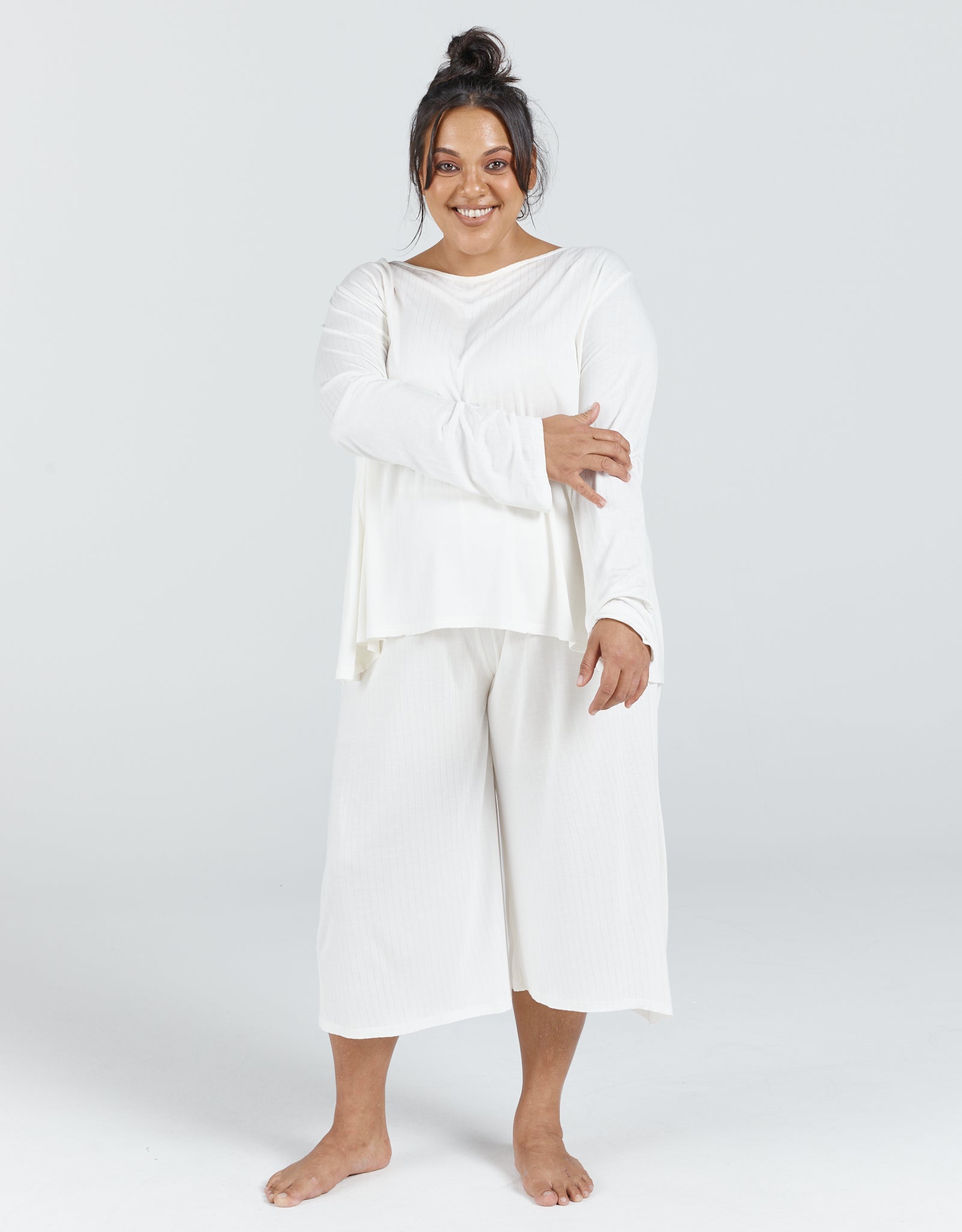 Essensual PJ Set showcased in pure white, featuring a loose-fitting long-sleeve top with boat neckline and flowing cropped palazzo-style pants. Comfortable sleepwear ensemble shown against a light gray background, emphasizing the relaxed, elegant cut and airy fabric.