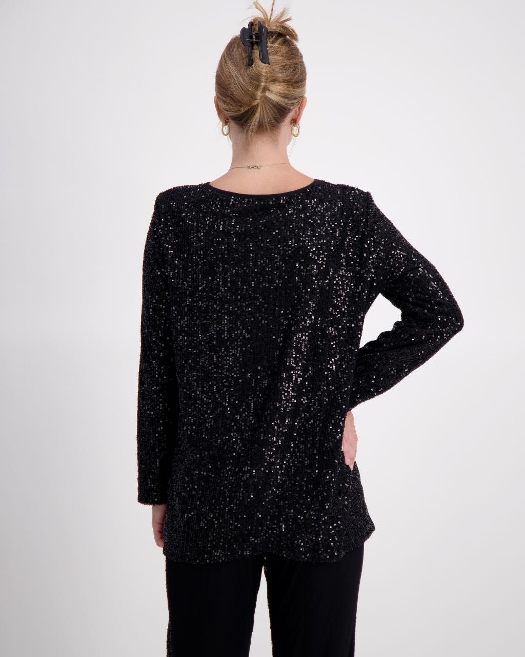 Tara V Neck Leaf Back Top shown from behind, featuring a shimmering black metallic glitter fabric with full-length sleeves. The distinctive leaf-pattern back design is elegantly displayed on a model wearing a casual updo hairstyle against a light gray background.