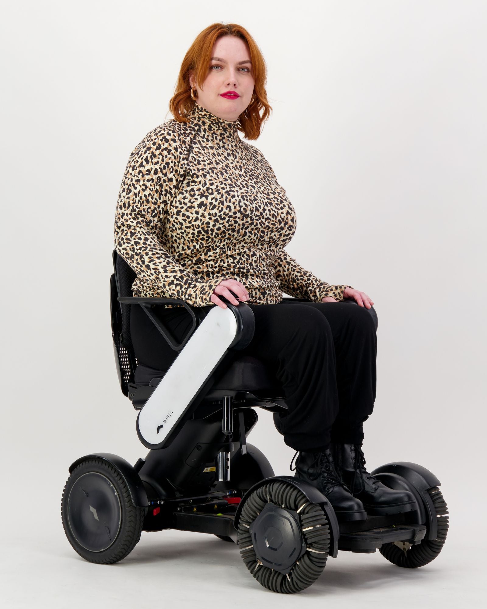 Maggie Thermal Top shown on a model seated in a modern white mobility device, featuring a stylish leopard print pattern with turtleneck design. The thermal top demonstrates adaptive wear comfort against a clean white background.