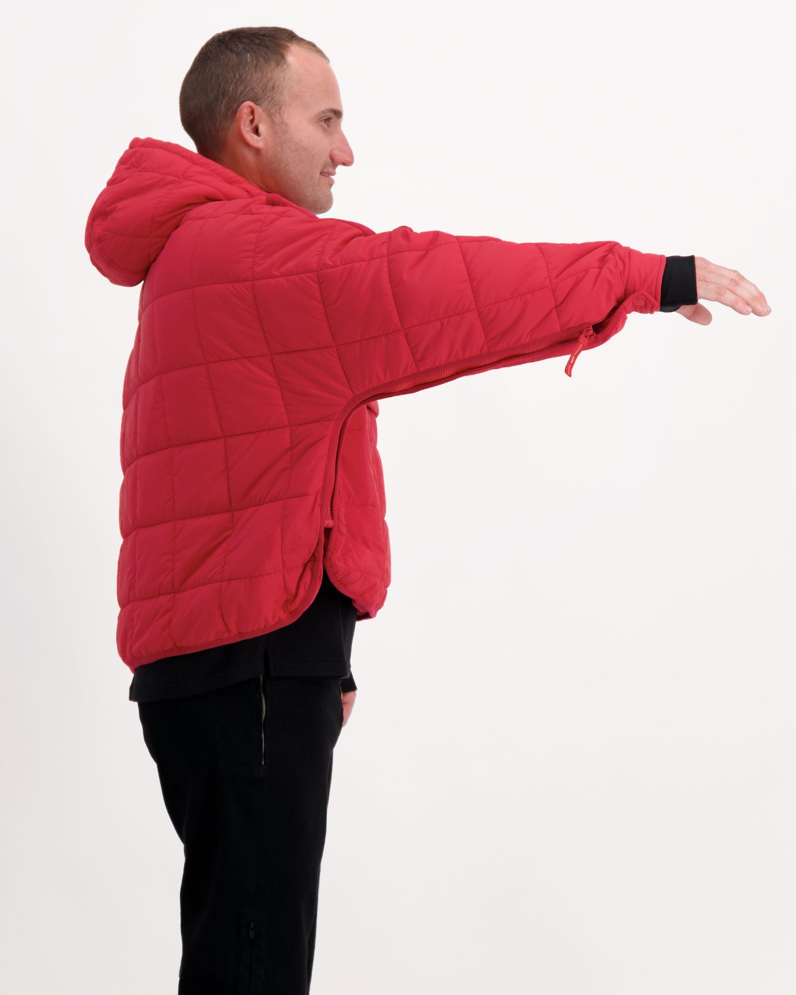 Elly Universal Puffer Jacket shown from side view in bright red, demonstrating adaptive design with quilted pattern. Model wearing black pants displays jacket's comfortable fit and extended arm mobility against white background, highlighting practical features for wheelchair users.