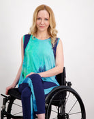 Lauren Sleeveless Physio Top shown in vibrant turquoise and navy watercolor pattern, featuring a sleeveless design with a flowy silhouette. Model wearing top paired with navy leggings while seated. The adaptive athletic wear showcases elegant draping and comfort-focused design.