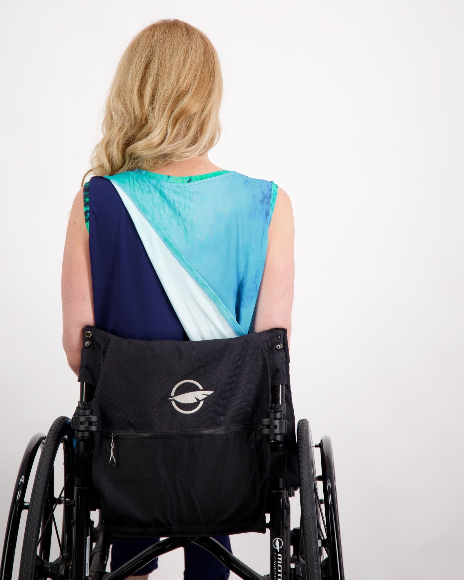 Back view of Lauren Sleeveless Physio Top featuring a stylish color-block design in navy and turquoise, shown worn in a wheelchair. The signature leaf pattern detail is visible on the back, highlighting the sleeveless athletic design perfect for exercise and physiotherapy sessions.