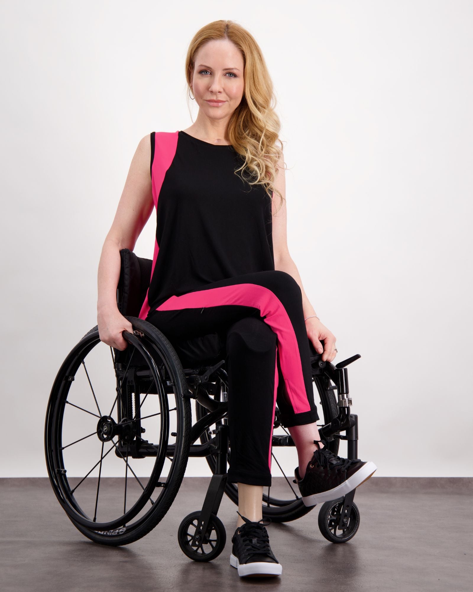 Lauren Sleeveless Physio Top shown in black with vibrant pink accents, displayed on a seated model against a white background. The sleeveless design features modern color blocking and a relaxed fit, perfect for athletic and casual wear.