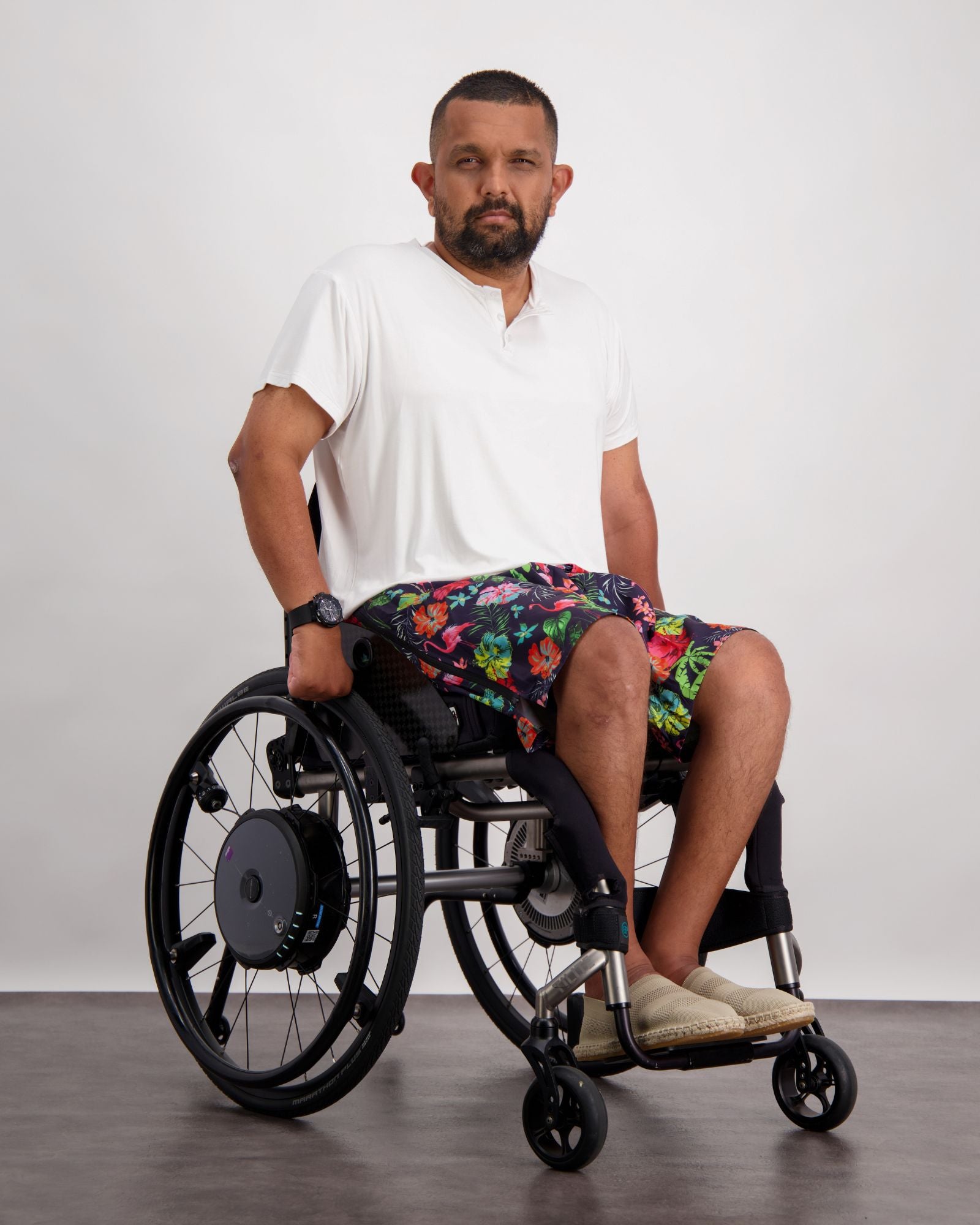 Nick A-Line T-Shirt shown on a wheelchair user against a light background. The white adaptive bamboo t-shirt is paired with colorful patterned shorts. The casual look demonstrates the shirt's versatility and comfortable fit while maintaining a stylish appearance.