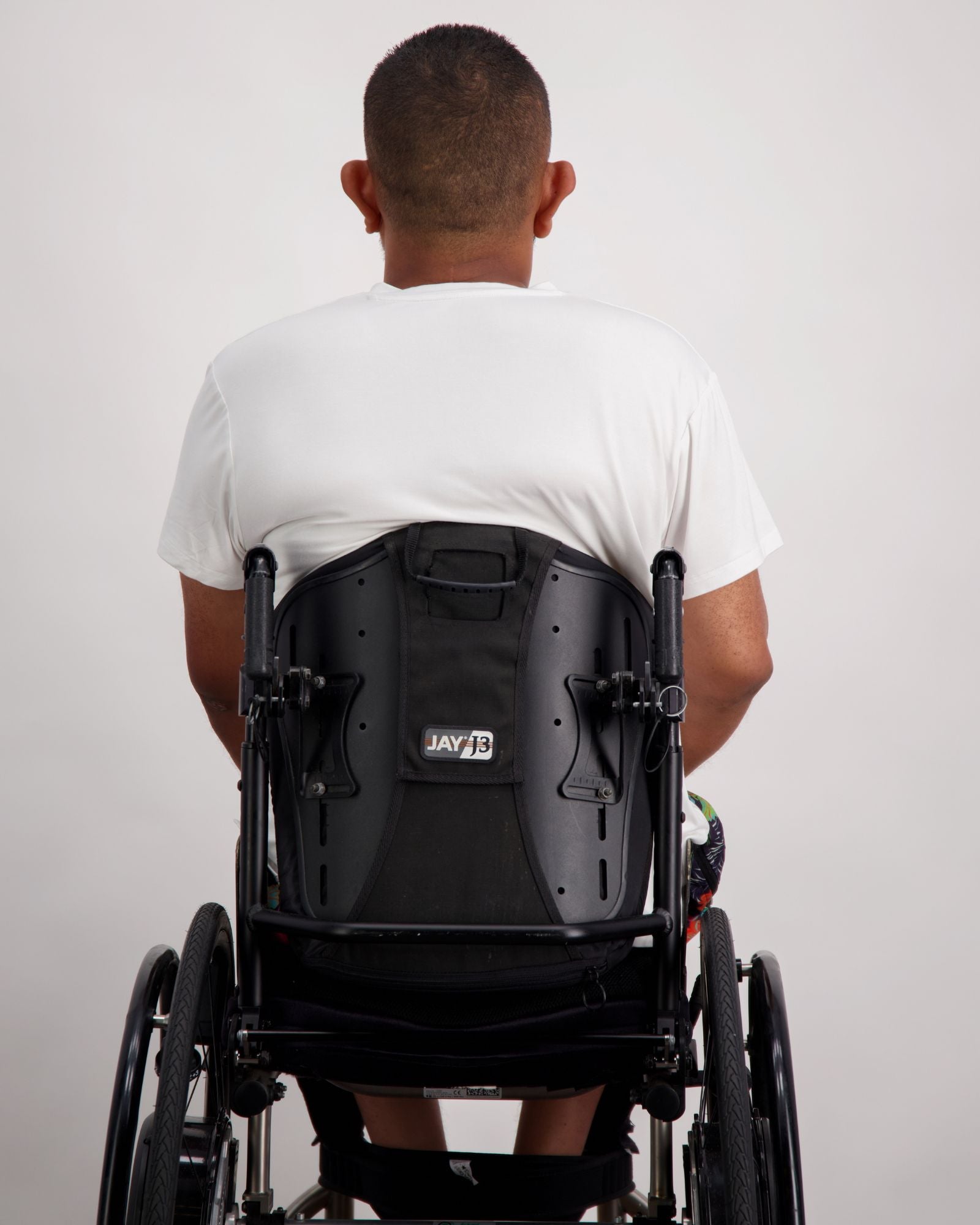 Back view of Nick A-Line T-Shirt in white bamboo fabric, shown on a person seated in a black wheelchair. The adaptive t-shirt demonstrates a comfortable, relaxed fit with clean lines and stretchy material suitable for everyday wear.