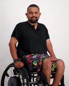 Nick A-Line T-Shirt in classic black bamboo fabric styled with colorful floral print shorts, showcasing adaptive wear comfort. Model seated in wheelchair demonstrates versatile casual wear suitable for both dressy and relaxed occasions. Product highlights sensory-friendly design and everyday comfort.