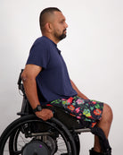 Navy Nick A-Line T-Shirt shown on a wheelchair user against white background, paired with floral print shorts. The adaptive bamboo shirt features a comfortable A-line cut, demonstrating its sensory-friendly design and versatile styling potential.