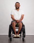 A person in a wheelchair wearing the Nick A-Line T-Shirt in white, paired with colorful patterned shorts and casual shoes. The adaptive bamboo t-shirt features a comfortable v-neck design, demonstrating its sensory-friendly fit against a neutral background.