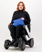 Matt Gender Neutral Puffer Vest shown folded into a bright blue travel pillow, displayed on a power wheelchair against a white background, demonstrating its adaptive design and convertible functionality.