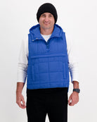 Matt Gender Neutral Puffer Vest shown in vibrant royal blue with quilted design, featuring a hooded collar and front pocket. The adaptive vest is displayed over a white long-sleeve shirt, demonstrating its lightweight layering capability and practical design for wheelchair users.