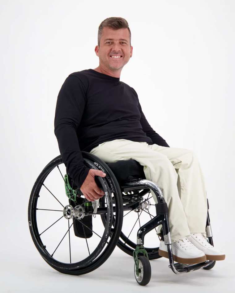 Mens Long Sleeve Leaf Back T-Shirt shown on model in wheelchair against white background, featuring classic black long sleeve design, paired with white pants and sneakers. Adaptive clothing demonstrates comfortable fit and easy accessibility.