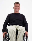 Mens Long Sleeve Leaf Back T-Shirt shown on a person seated in a wheelchair, wearing khaki pants against a white background. The black t-shirt features a classic crew neck design with long sleeves, demonstrating comfortable casual wear that's accessible and stylish.