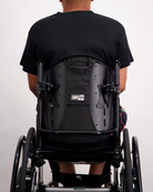 Nick A-Line Tee shown from behind on a wheelchair user, displaying the adaptive design with a clean black fabric against a white background. The shirt's A-line cut complements the seated position while maintaining a sleek, modern silhouette.