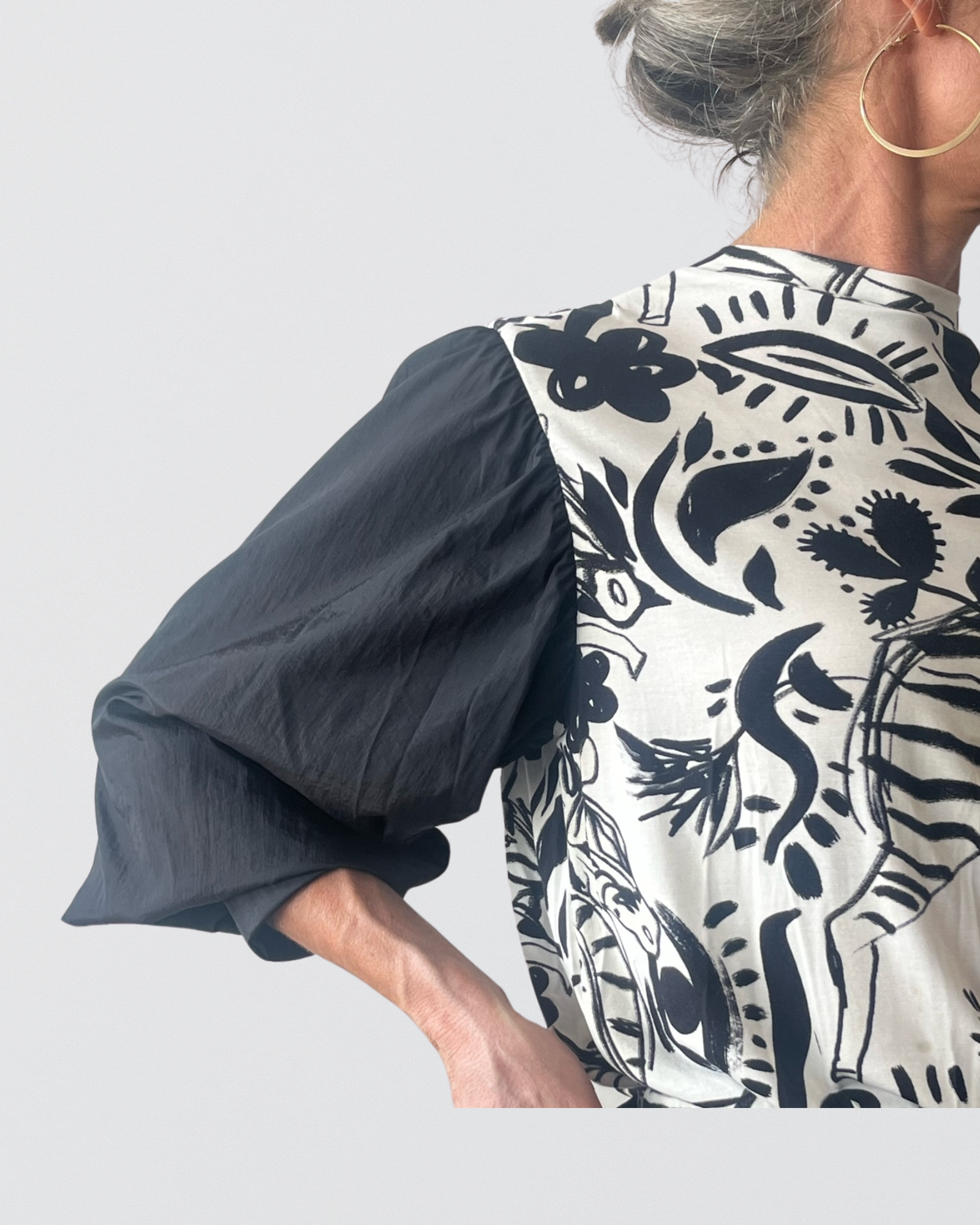 Tracey Adaptive Prism Back Top featuring dramatic black puff sleeves contrasting with a white back panel adorned with bold black floral and botanical prints, shown from a side-back angle against a light background, highlighting the garment's romantic design elements.