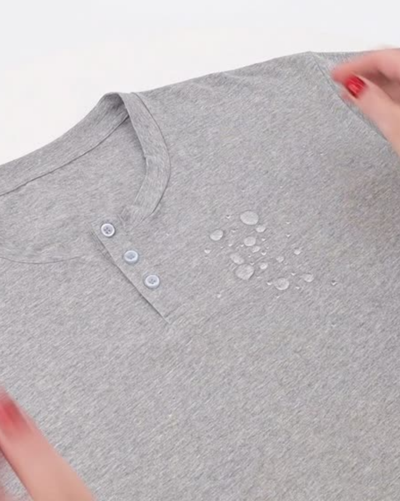 Nick A-Line Tee in heather gray featuring spill-resistant technology, with water droplets beading on the surface. Close-up view showing three-button henley neckline detail and the fabric's water-repellent properties in action.