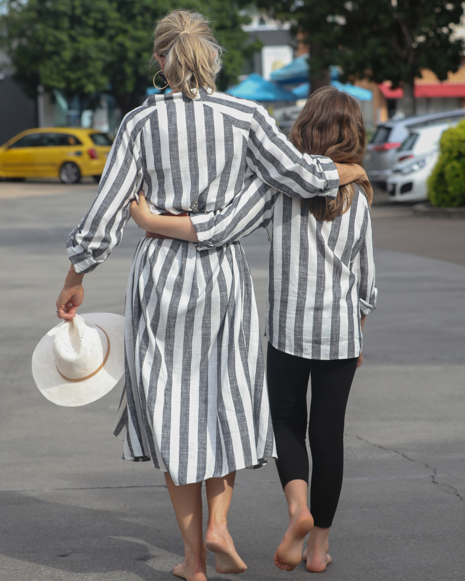 Sapphire Magnetic Shirt Dress shown in casual outdoor setting, featuring elegant black and white vertical stripes, flowing midi length design, with relaxed long sleeves. Summer hat accessory visible, demonstrating the dress's versatile styling potential and comfortable linen fabric.