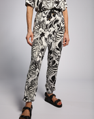 Roisin Adaptive Slouch Pants featuring a bold black and white zebra print pattern, tapered legs with elastic cuffs, styled with black platform sandals. The pants showcase a relaxed fit and Smart Access design in comfortable bamboo fabric against a grey studio background.