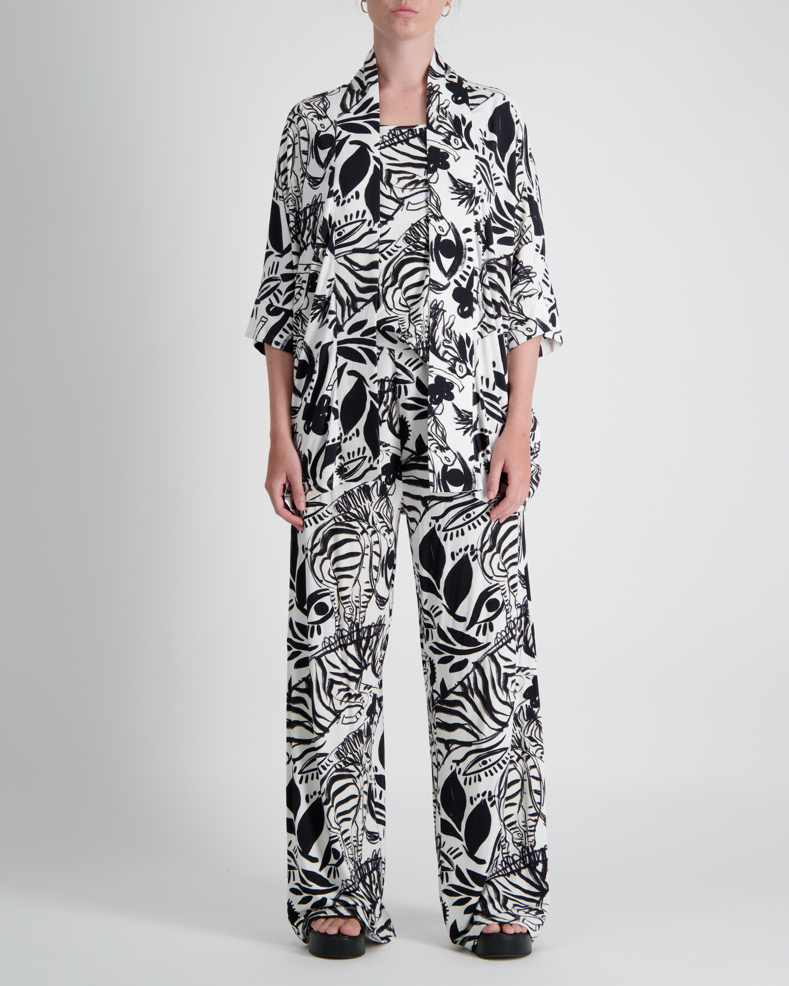 Jessie Wide Leg Pant shown in striking black and white abstract floral print pattern. Model wearing matching top with three-quarter sleeves. Wide-leg silhouette features comfortable, flowing design against light studio background.