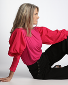 Tracey Adaptive Prism Back Top shown in vibrant pink with romantic puff sleeves and fitted cuffs, paired with black pants. Side view presents the top's elegant draping and sustainable bamboo fabric texture against a white background.