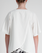 Lilli Leaf Back T-Shirt shown from behind, featuring a unique split-back design in crisp white bamboo fabric, with overlapping leaf-shaped panels and relaxed elbow-length sleeves against a light gray background, highlighting its adaptive and sensory-friendly construction