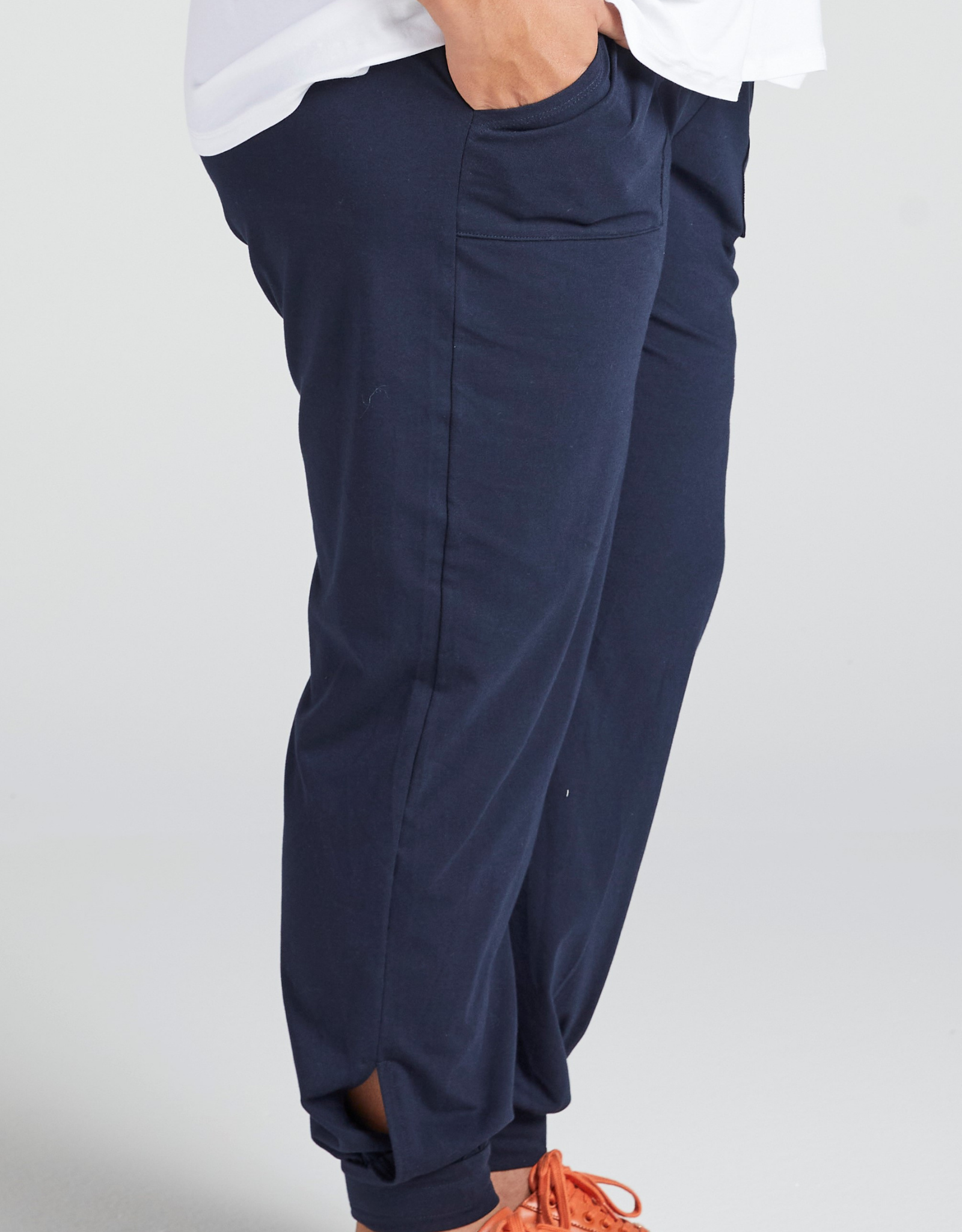 Tapered Track Pants with Adjustable Cuff shown in navy blue, featuring a relaxed fit with side pocket detail and elastic cuffs at ankles. Mid-rise waistband visible with white shirt partially tucked in, styled with orange sneaker laces.