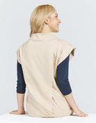 Leaf Back Dress shown from behind featuring a natural undyed cotton fabric with unique leaf-shaped back design. Model wearing cream-colored sleeveless top with navy long sleeves underneath, showcasing the comfortable, stretchy material and high neckline against a white background.