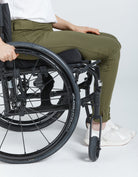 Seated Leggings shown on a wheelchair user, featuring olive green color and stretchy bamboo spandex fabric. Close-up view highlighting comfortable fit and accessibility while seated, paired with white sneakers and casual white top.