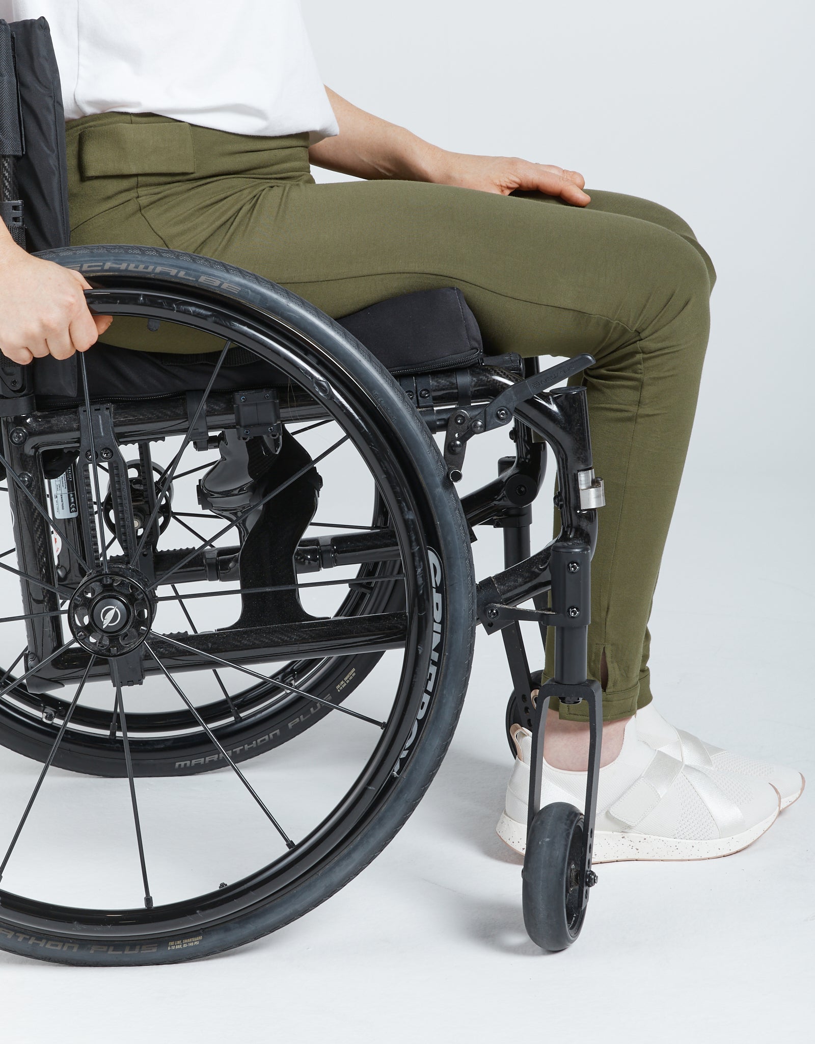 Seated Legging for SP Catheter shown on a wheelchair user wearing olive green adaptive leggings with reinforced openings. Close-up view highlighting comfortable fit, bamboo fabric texture, and specialized design features including catheter access points.