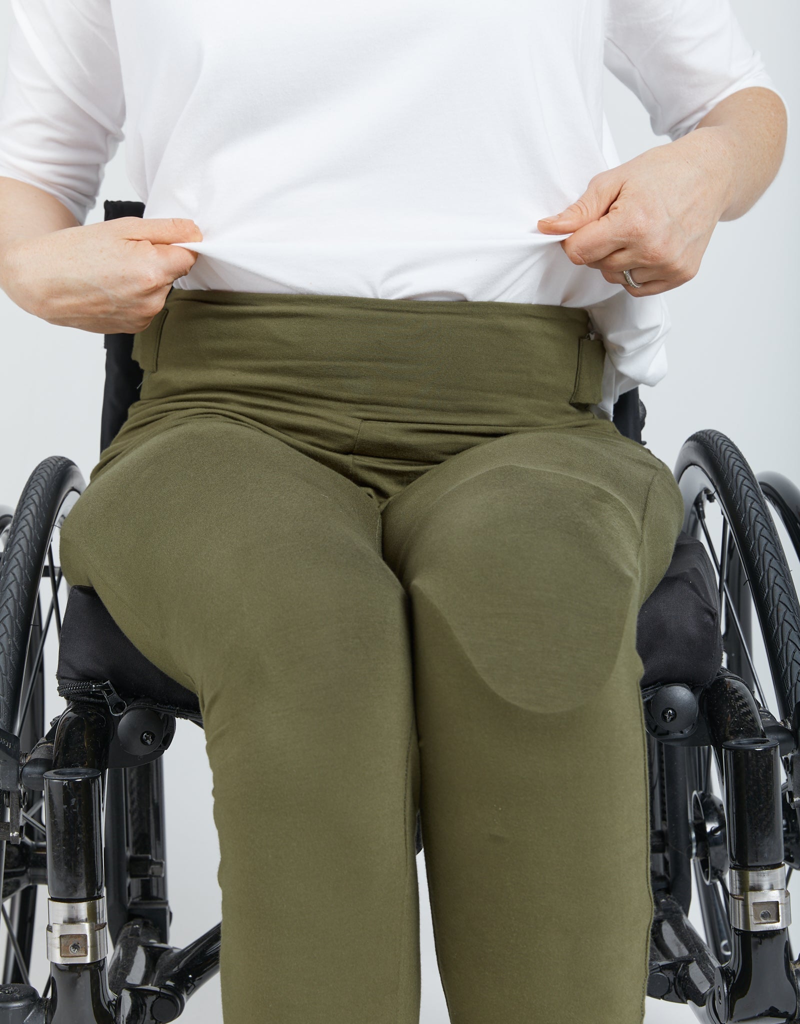 Seated Leggings shown in olive green color on a wheelchair user wearing a white top, demonstrating the comfortable fit and easy-to-wear design of the adaptive clothing. The leggings feature a high waistband and smooth bamboo fabric texture.