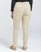 Seated Stretch Pant shown from back view in beige color with elastic waistband, straight-leg design, and full-length fit. Model wearing black top and tan sandals against white background, demonstrating comfortable, tailored silhouette ideal for wheelchair users.