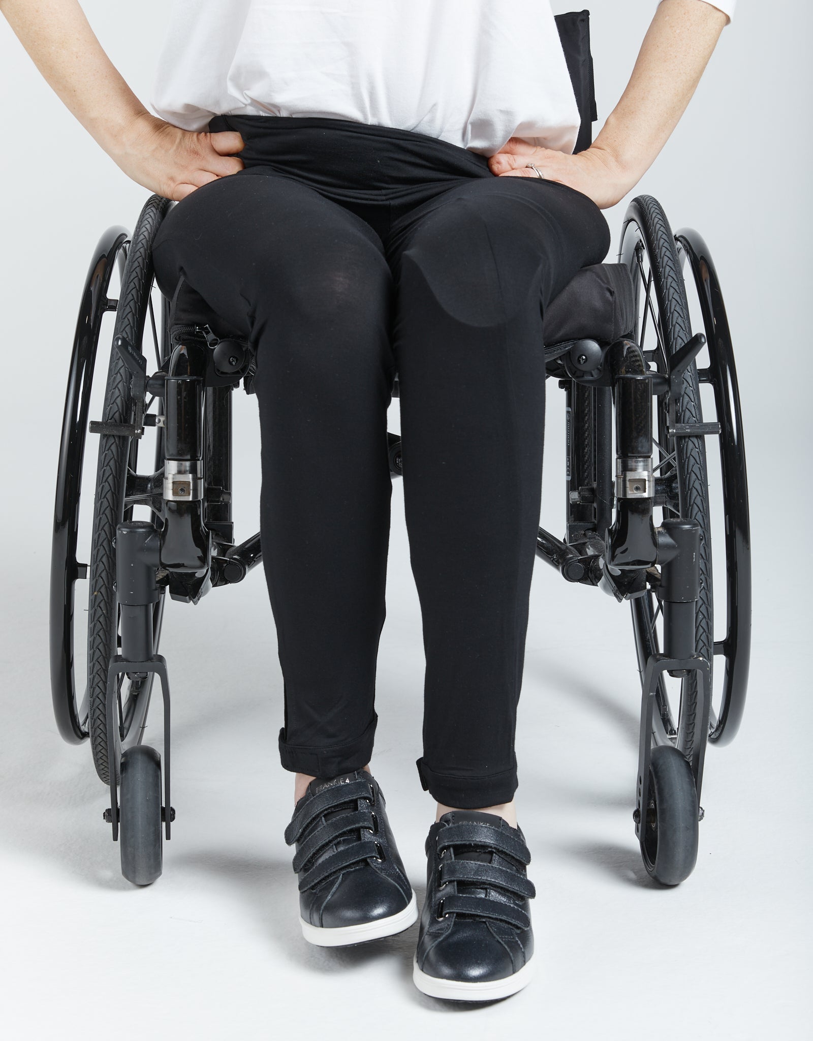 Seated Legging for SP Catheter shown on a wheelchair user wearing black adaptive leggings with specialized loops and openings, paired with a white top and black sneakers, demonstrating comfortable fit and accessibility features