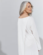 Essensual PJ Dress shown in elegant white fabric with long sleeves and boat neckline, photographed against a light grey background. The sleepwear features a flowing, comfortable design that emphasizes both style and functionality for peaceful rest.