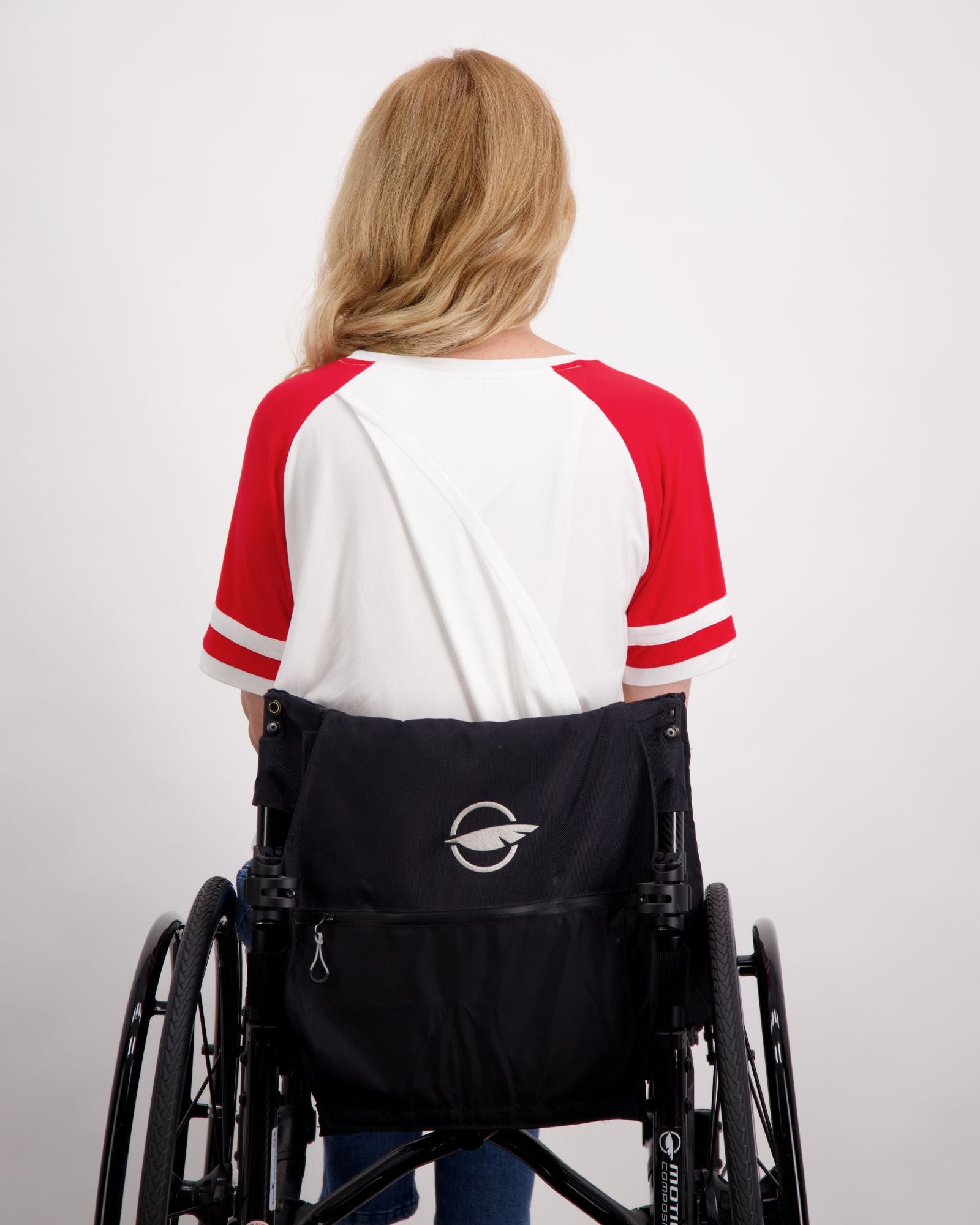 Lisa Raglan Leaf Back T-Shirt shown from behind on someone seated in a wheelchair, featuring a classic white body with red raglan sleeves and stripe details. The shirt demonstrates the casual, sporty design with a relaxed fit against a light background.