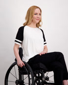 Lisa Raglan Leaf Back T-Shirt shown in classic black and white design with contrasting stripe details on sleeves. Model seated wearing casual ensemble demonstrating comfortable fit and versatile styling of this sporty raglan tee.