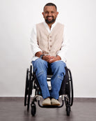 Stephen Seated Jeans modeled in wheelchair, featuring comfortable denim paired with crisp white shirt and beige waistcoat, showcasing adaptive fashion wear against neutral background